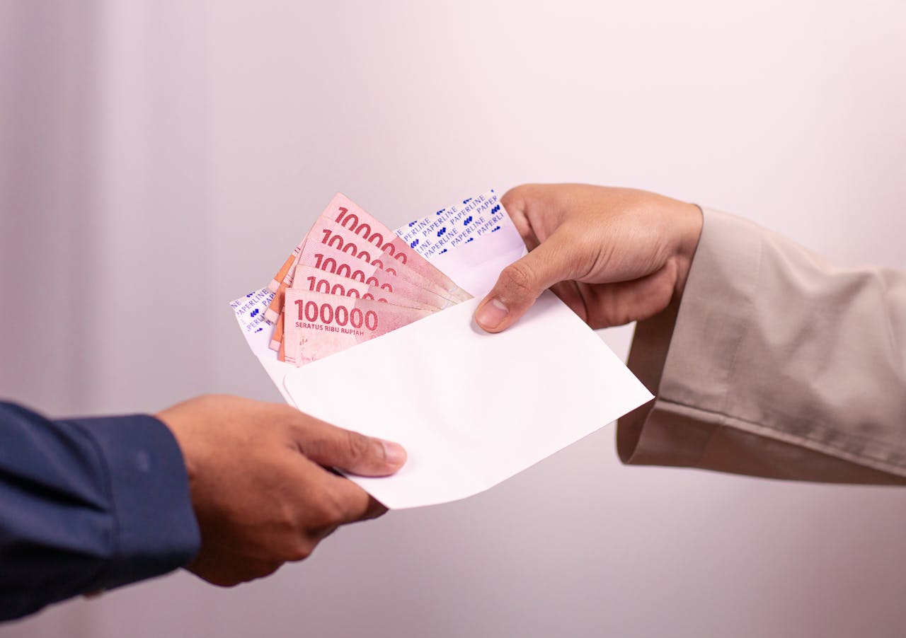 services-03 Hands giving and receiving Indonesian rupiah in an envelope, symbolizing financial transaction.