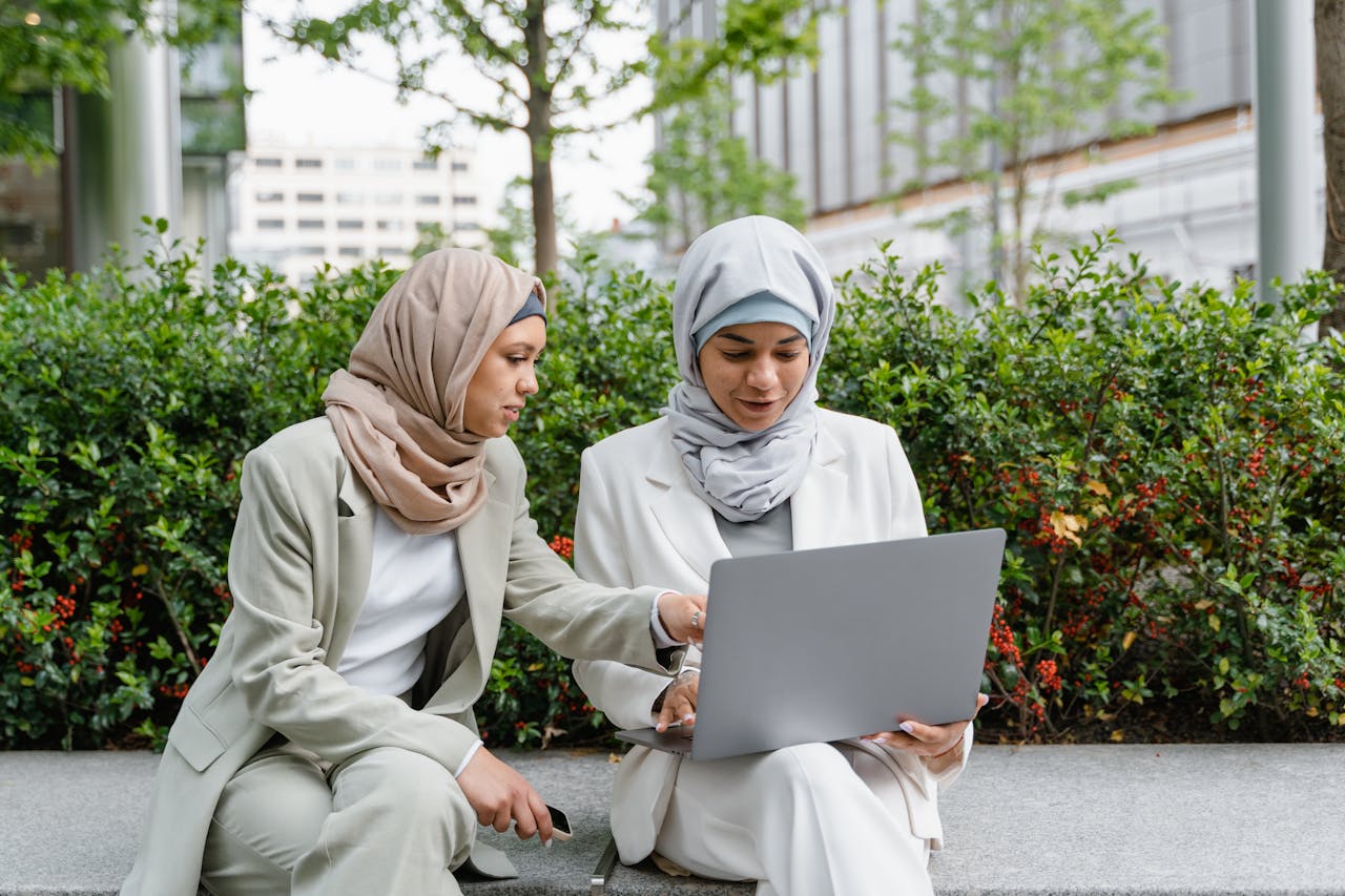 services-01 Two Muslim women in business attire working together outside on a laptop, focusing on collaboration and technology.